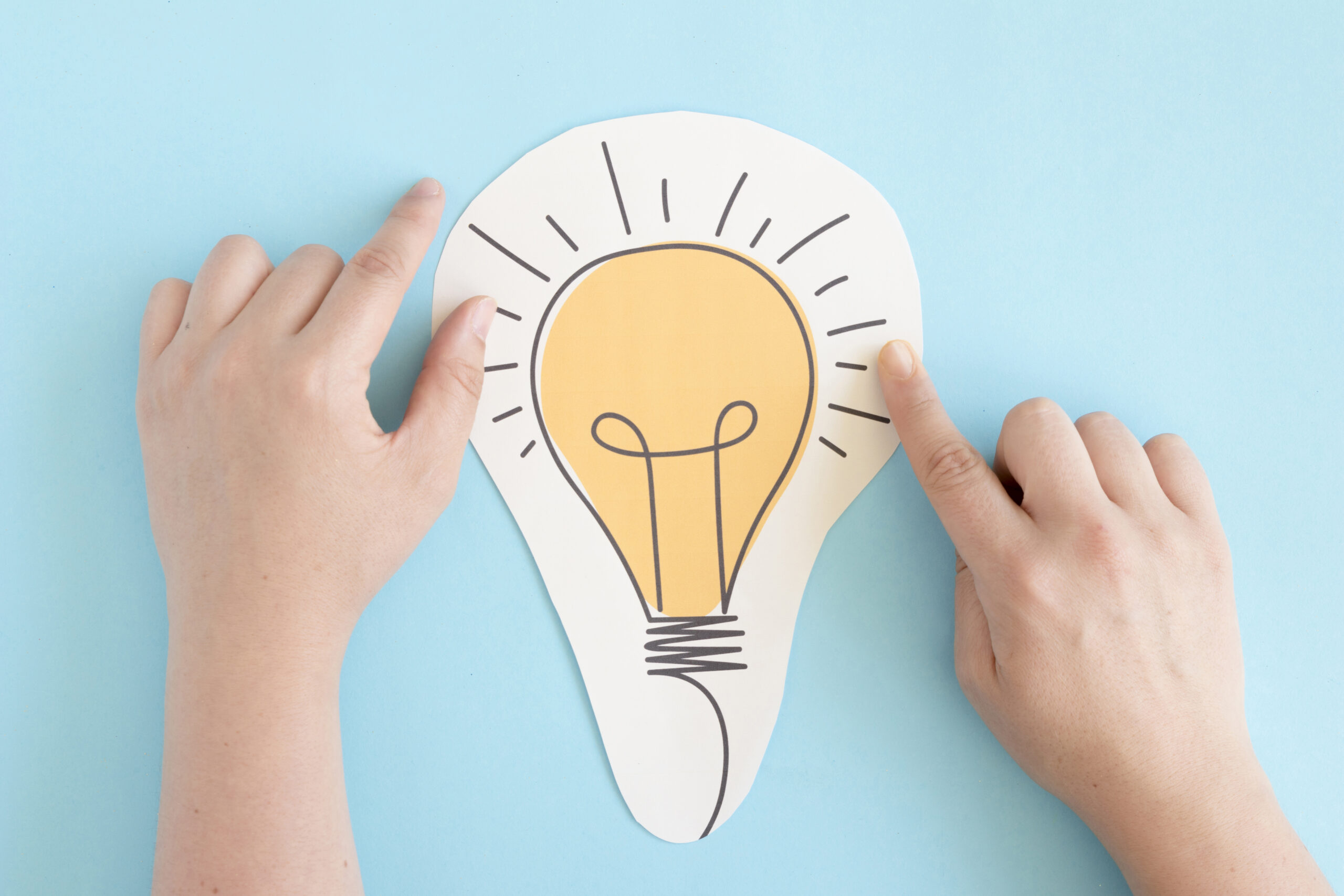 hand touching cut out paper bulb blue background